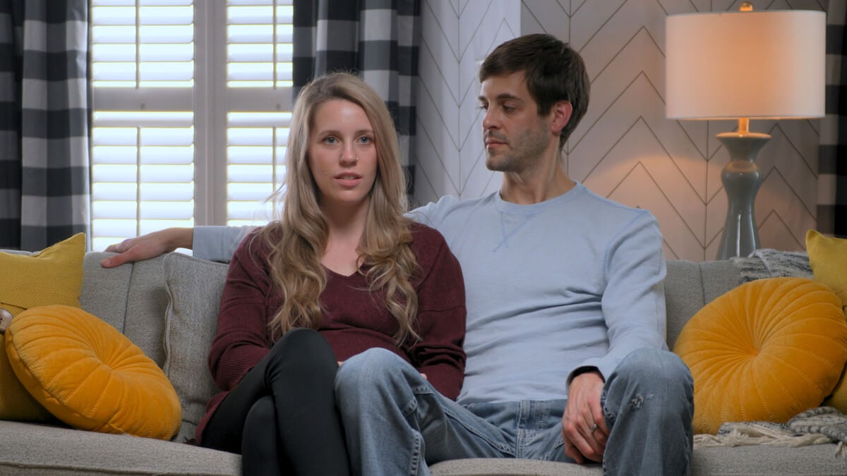 Jill Duggar Dillard and Derick Dillard sitting on a couch in Prime Video docuseries 'Shiny Happy People: Duggar Family Secrets'