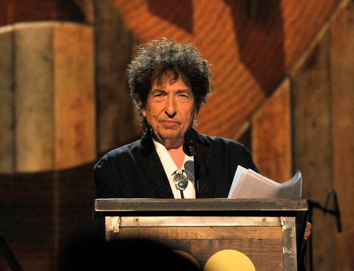 Bob Dylan stands behind a podium and holds a stack of papers.