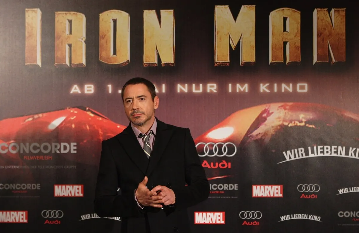 Robert Downey Jr posing in front of an Iron Man poster in a suit.