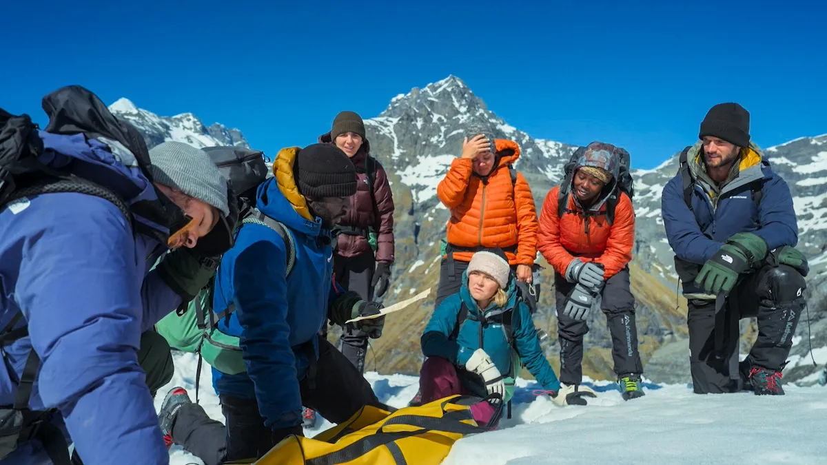 Group of seven cast members gather around a yellow bundle in episode 8 of 'The Summit'