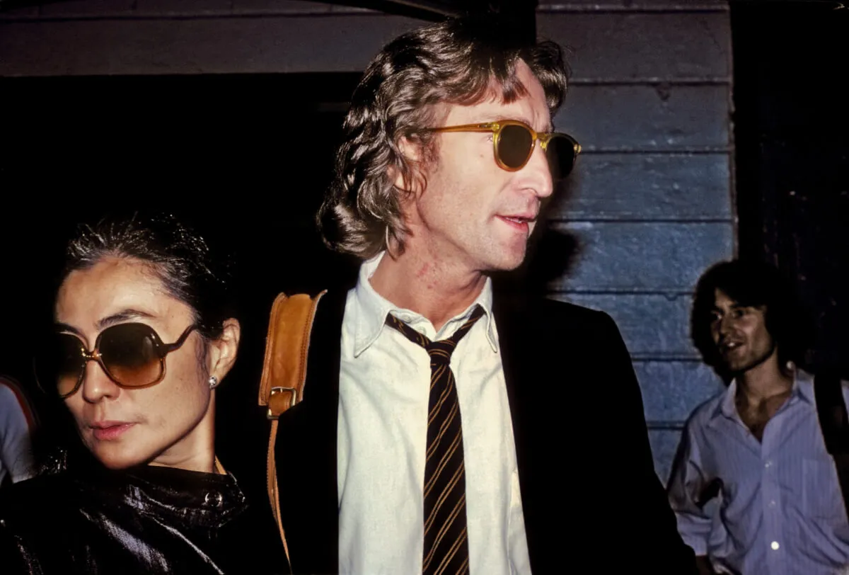 Yoko Ono and John Lennon wears sunglasses and look in different directions.